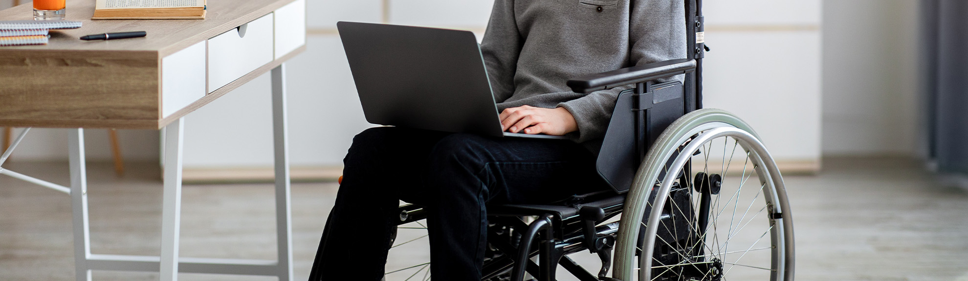 Disabled teen boy in wheelchair doing online homework on laptop indoors